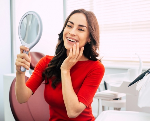 Woman looking at smile in mirror after dental checkup and teeth cleaning