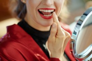 Woman inspecting her teeth in a handheld mirror.